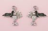 Pair of ornate earrings with floral and leaf designs on a pink background