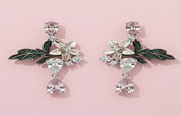Pair of ornate earrings with floral and leaf designs on a pink background