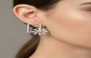 Silver square-shaped earring worn by a person with a neutral background