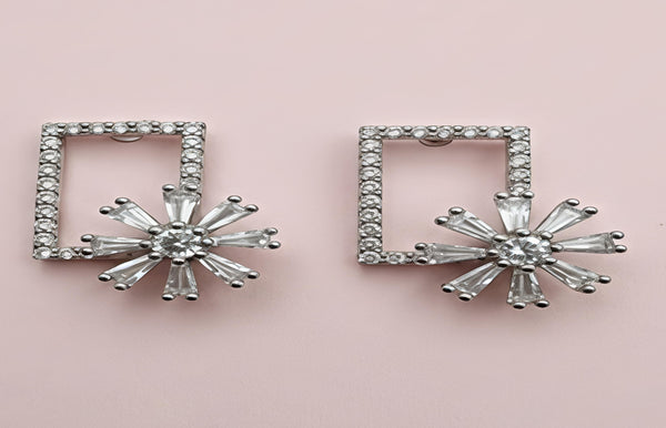 Pair of silver square-framed earrings with starburst design on a pink background