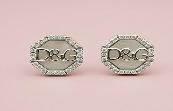 Pair of silver earrings with 'D&G' logo on a pink background