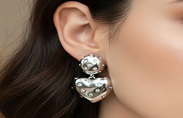 Close-up of a person wearing silver heart-shaped earrings with a blurred background
