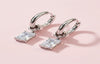 Silver hoop earrings with square-cut gemstones on a pink background