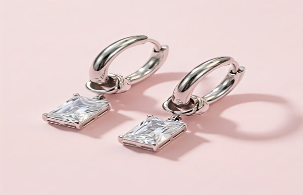 Silver hoop earrings with square-cut gemstones on a pink background