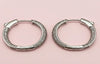 Pair of silver hoop earrings with gemstone accents on a pink background