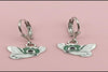 Butterfly-shaped earrings with green accents on a pink background