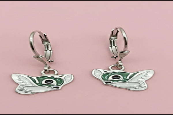 Butterfly-shaped earrings with green accents on a pink background