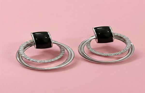 Pair of silver hoop earrings with black gemstones on a pink background
