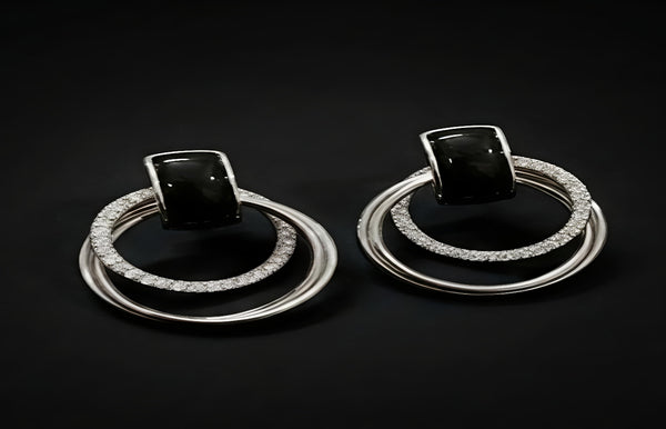 Pair of earrings with black gemstones and silver rings on a dark background