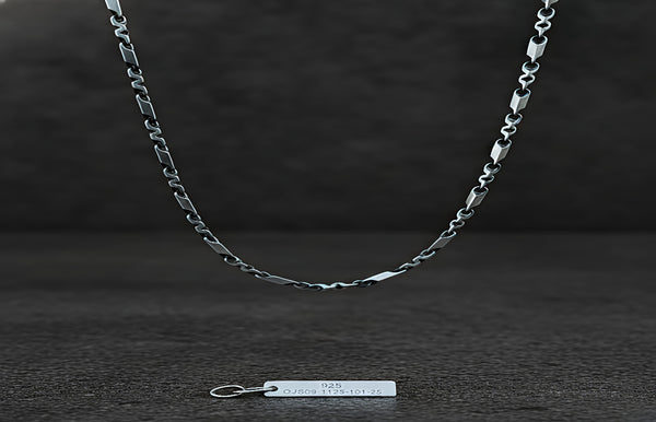 Silver chain necklace on a dark wooden surface with a tag below.