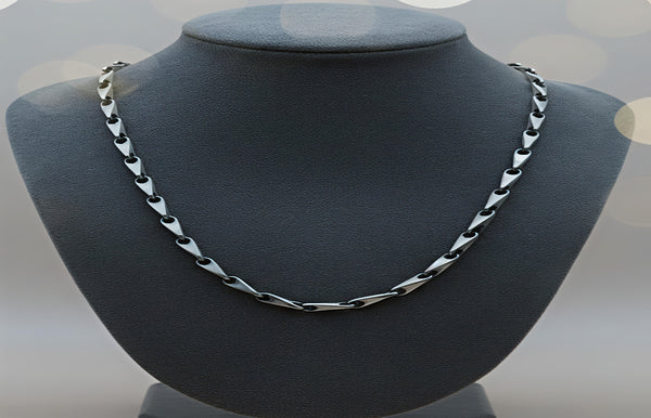 Silver chain necklace on a gray mannequin bust with a blurred light gray background