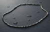 Silver necklace on a dark textured surface with water droplets