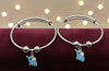 Two silver bangles with blue elephant charms on a dark surface with blurred lights in the background.