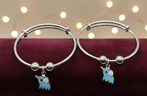 Two silver bangles with blue elephant charms on a dark surface with blurred lights in the background.