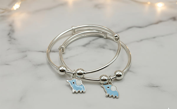 Silver bangle with blue bird charms on a marble surface