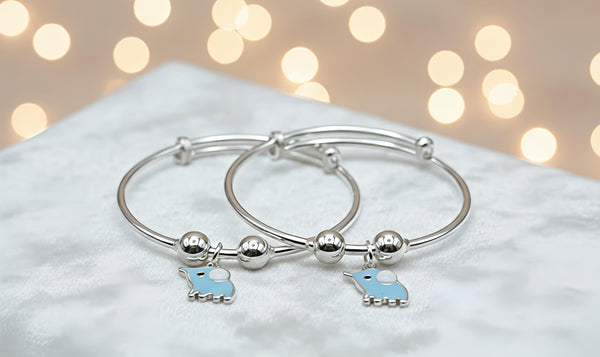 Silver bangle with blue elephant charms on a soft surface with blurred lights in the background